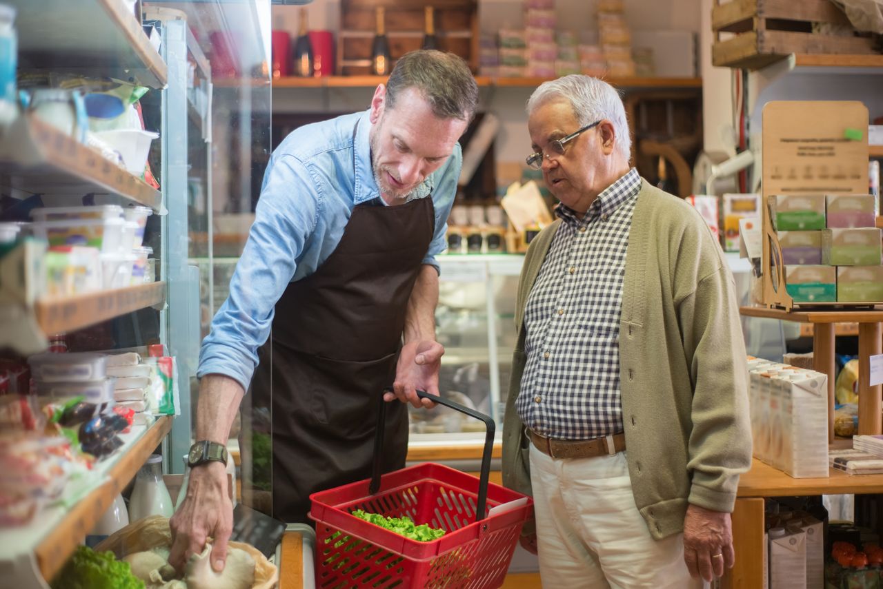 our-mission A salesman helps an elderly man with shopping in a local grocery store.